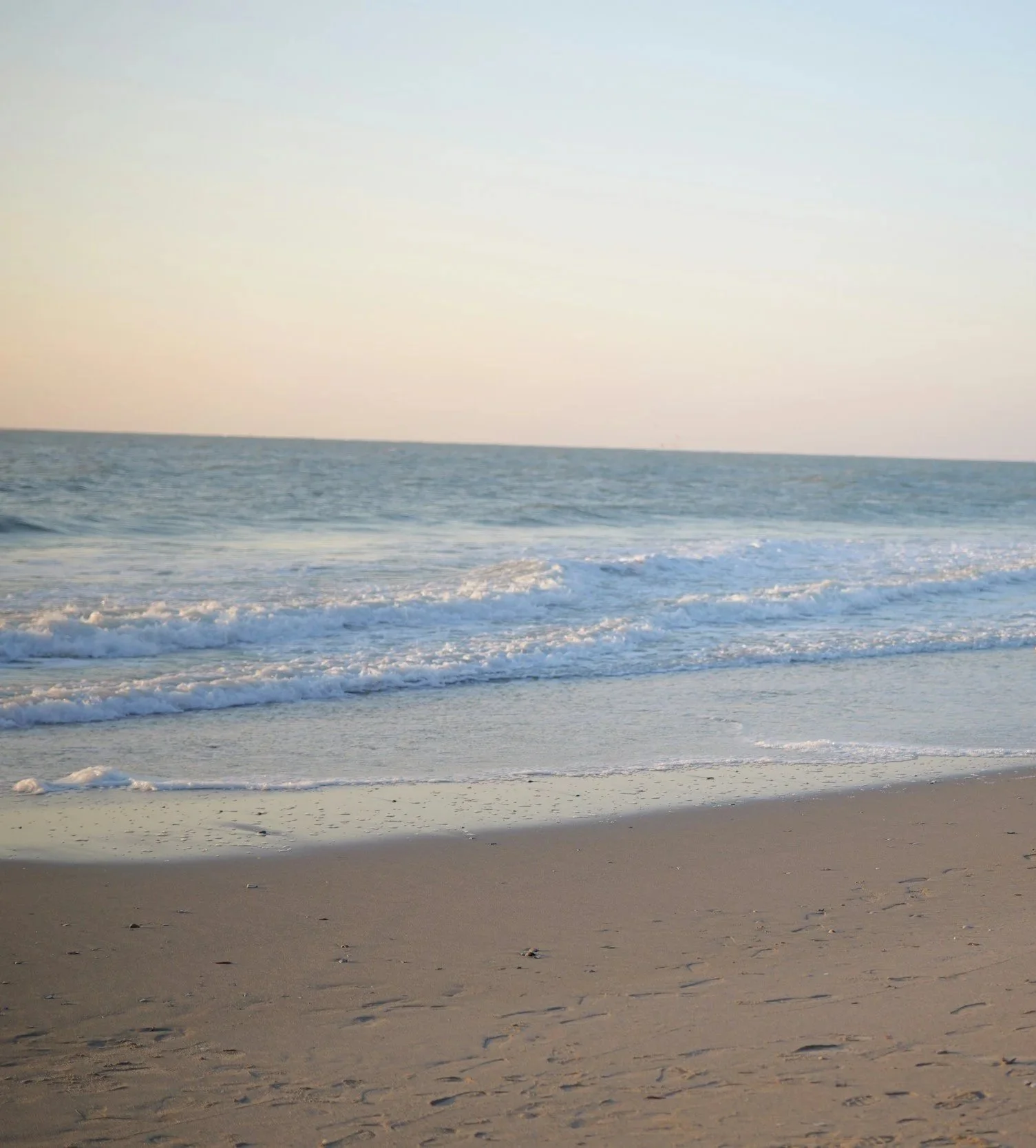 Sandy beach in Surfside Beach, SC with gentle waves along the shoreline and a calm ocean stretching to the horizon under a clear sky