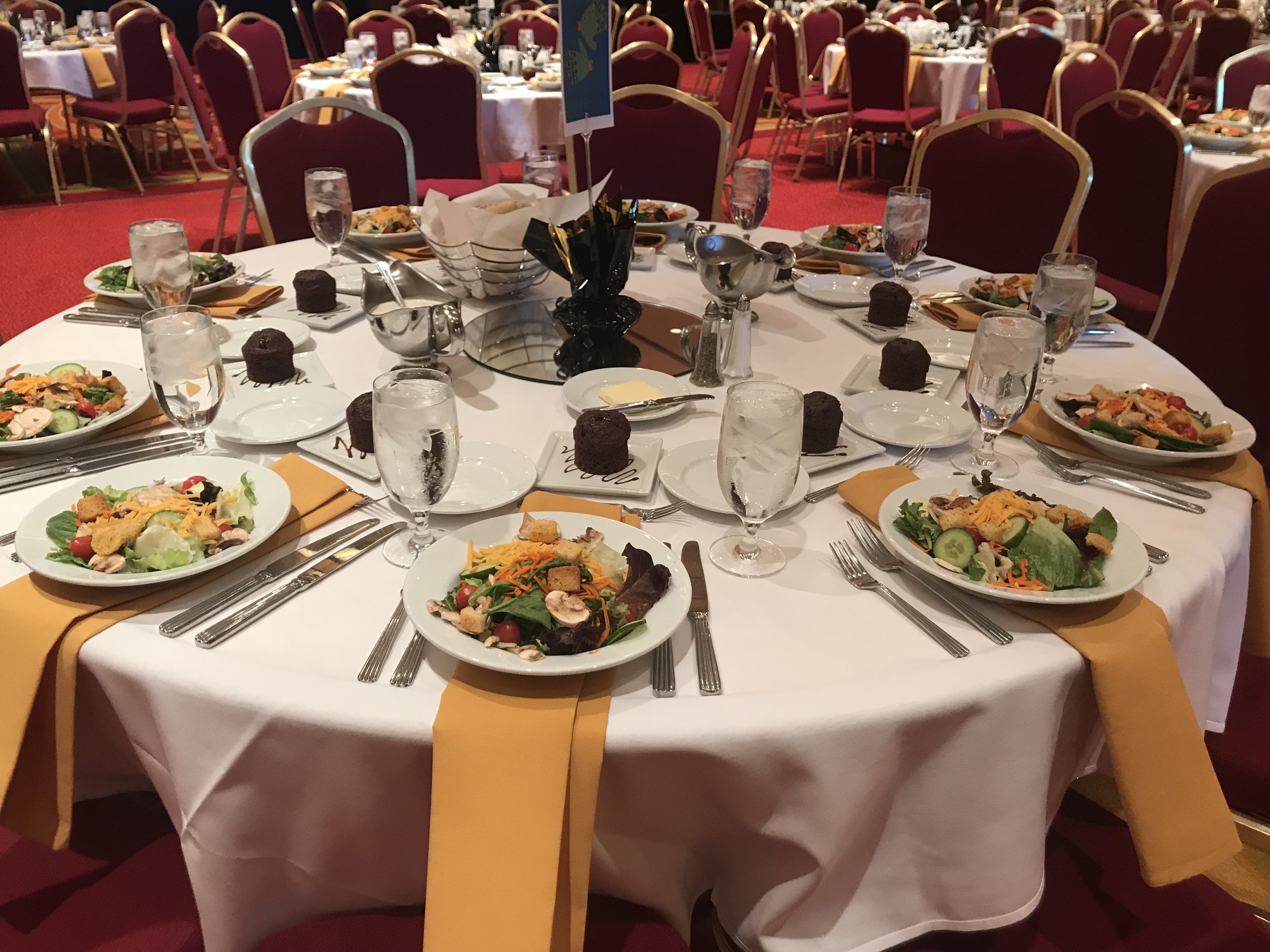 Corporate dinner set up with preset salad and desserts.  Corporate banquet set with yellow napkins