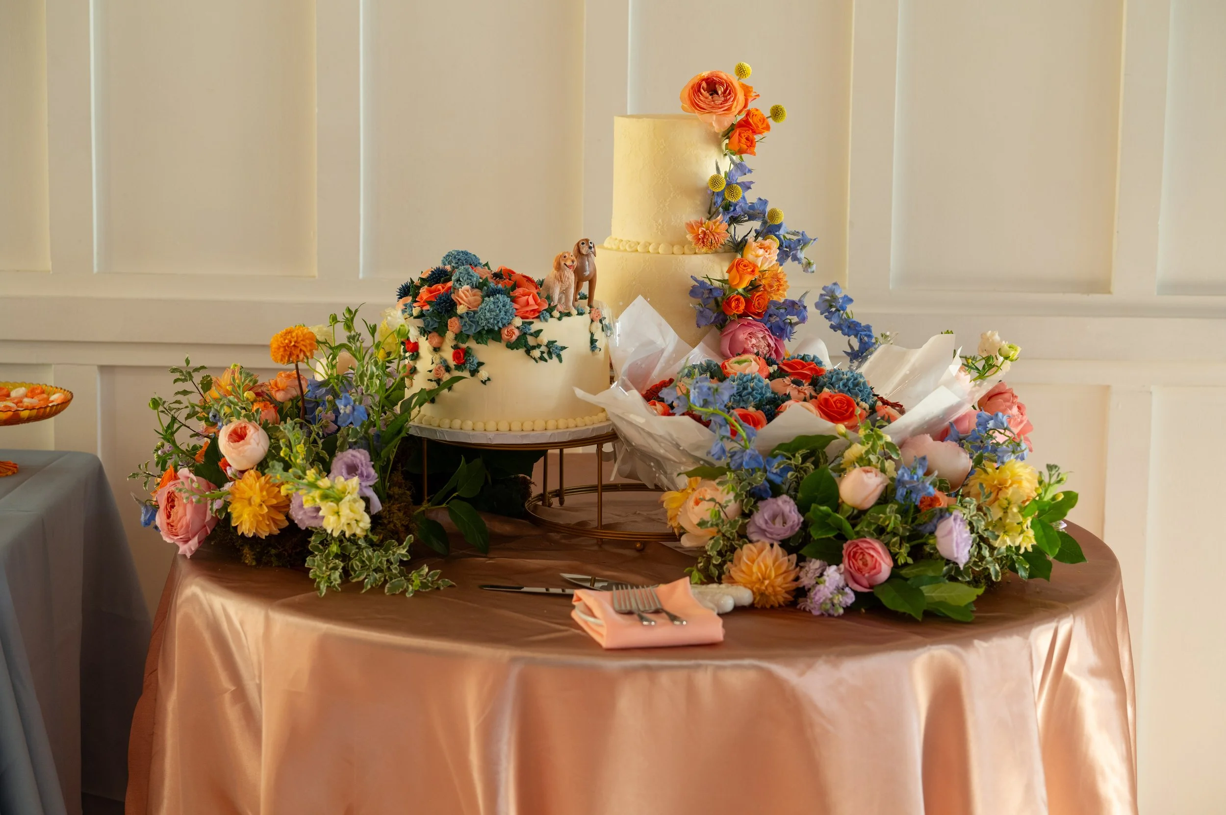 wedding cake display featuring three different cakes and bright colorful floral wreath