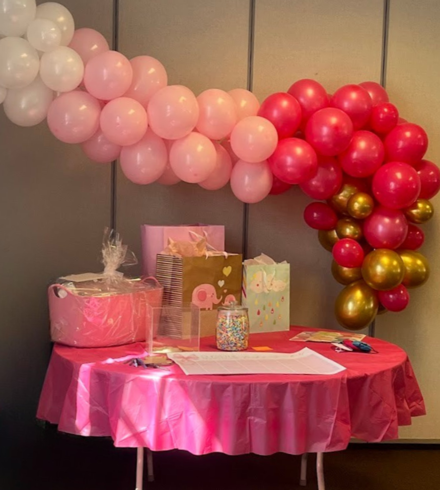 Bright pink gift table set up for baby girl baby shower with monochromatic pink balloon arch