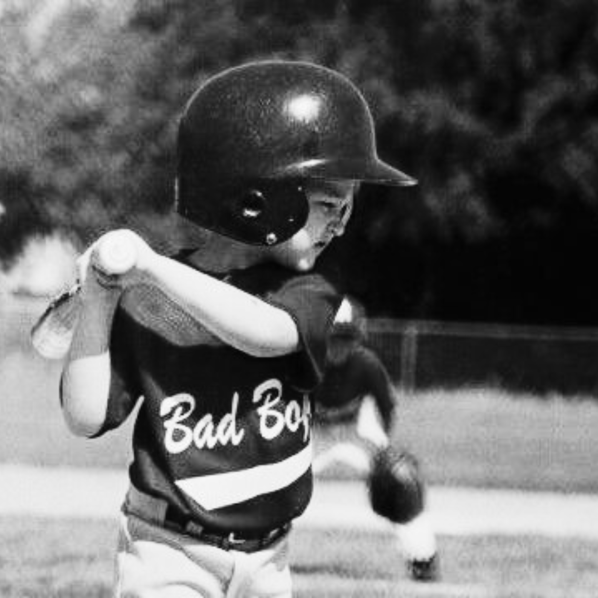 A young baseball player wearing a helmet and jersey with "Bad Boy" written on it, holding a bat, on a baseball field.