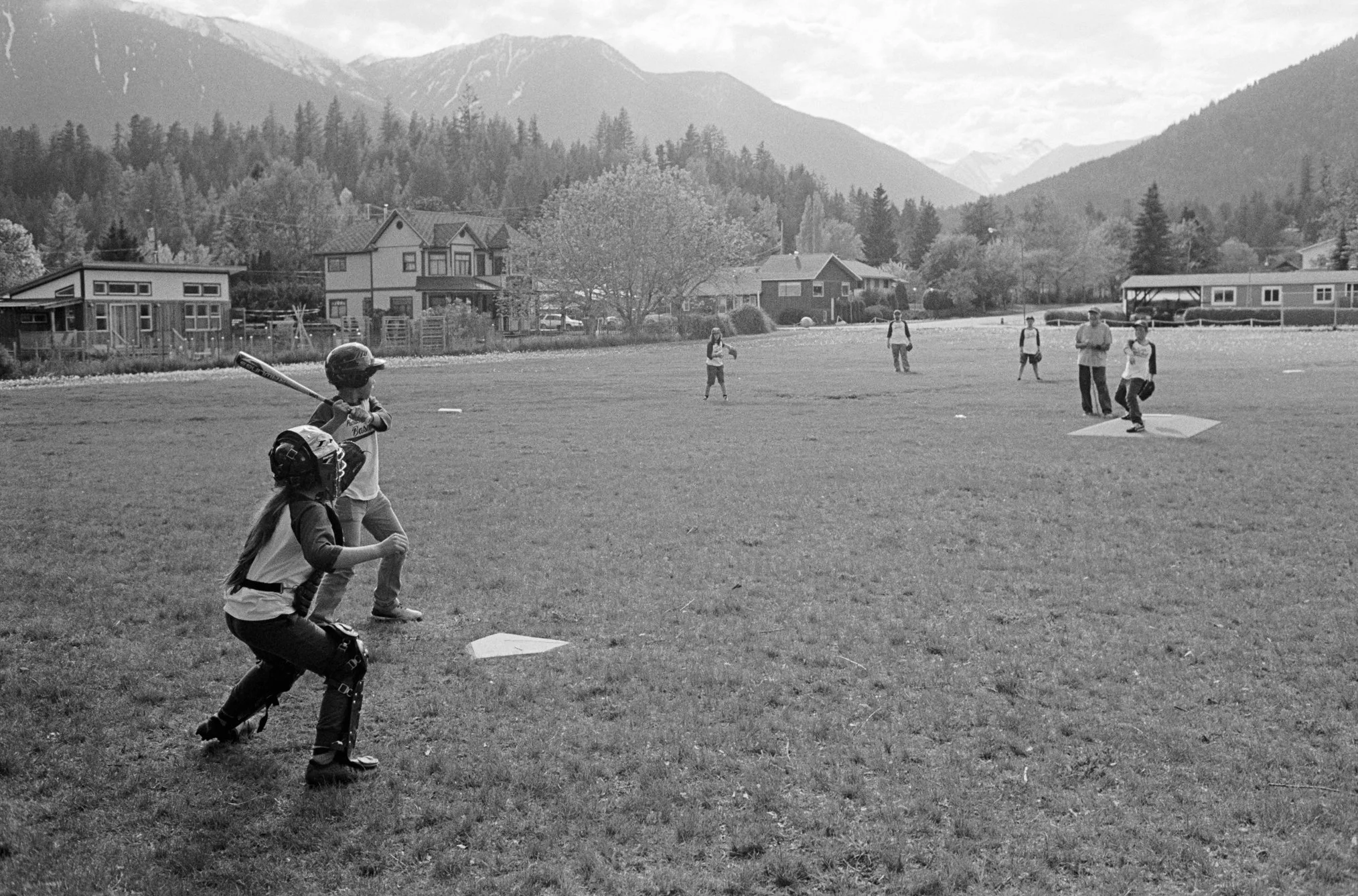 Children practicing baseball on a field with mountains and houses in the background.