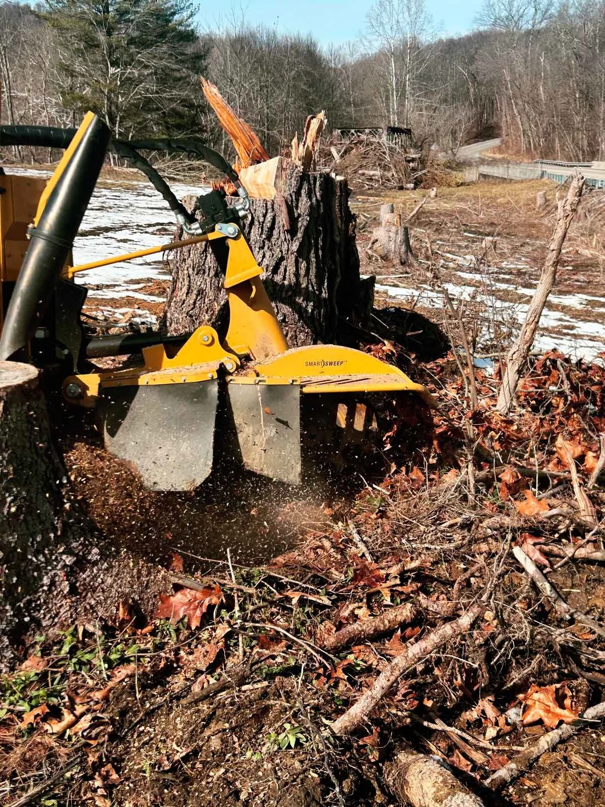 Yellow stump grinding machine actively throwing dirt and debris from stump and ground.