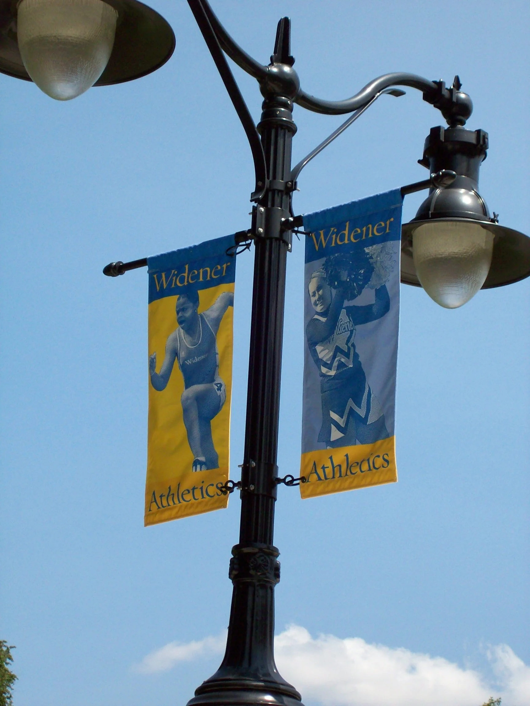 Street lamp post with banners featuring female athletes, including the word 'Widener' and 'Athletics', under a sunny sky.