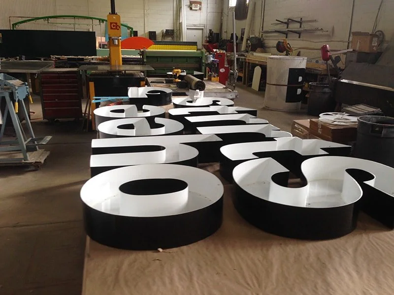 Large black and white letter-shaped signs or sculptures on a work table in a workshop or manufacturing space.