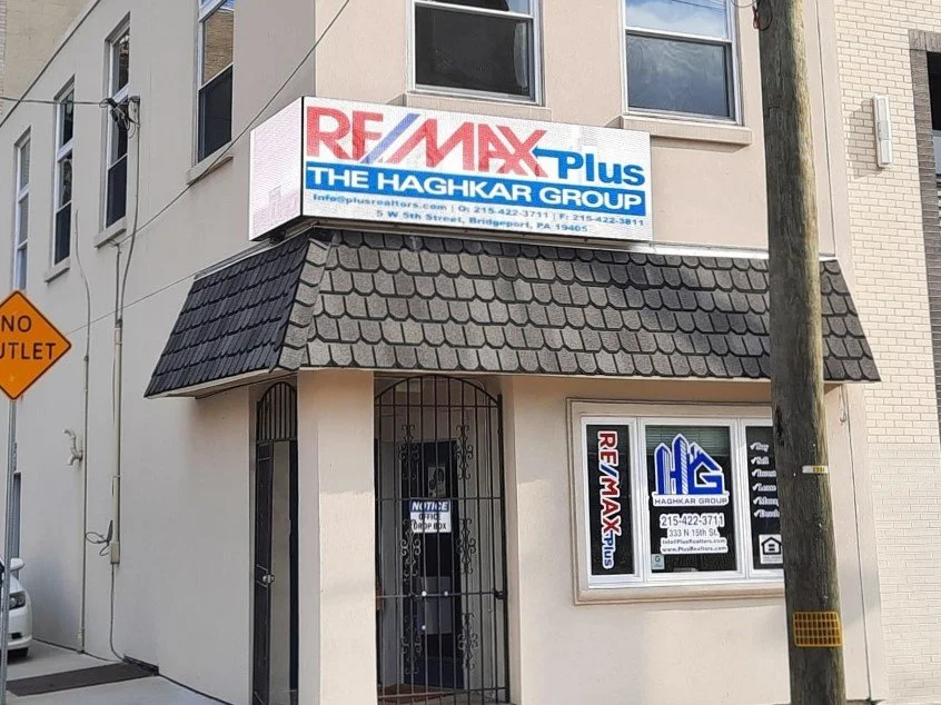 Street corner with a building bearing a RE/MAX Plus sign, showing real estate branding and contact info, and a nearby street sign reading 'No Outlet'.