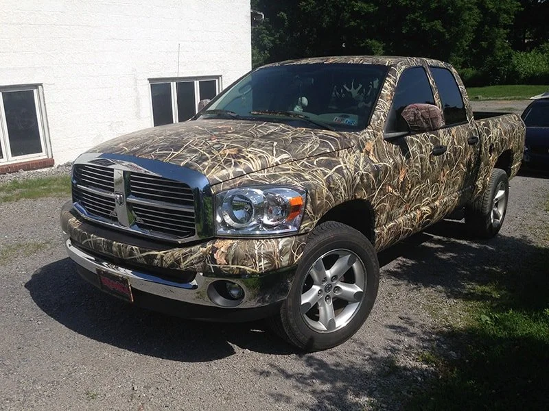 A camouflaged Dodge Ram pickup truck parked outdoors on a gravel surface.
