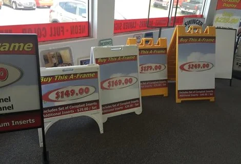 Display signs advertising A-Frames for sale at $149.00, $169.00, and $249.00, with product details about coroplast inserts and instructions included.