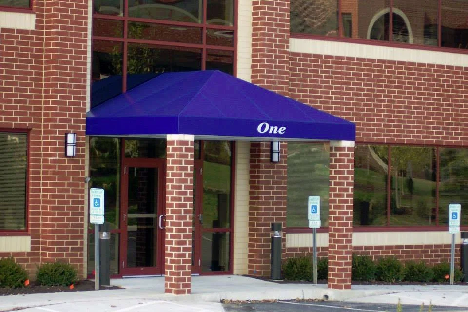 Blue canopy with the word 'One' above the entrance of a brick building, with accessible parking spaces marked for handicapped parking.