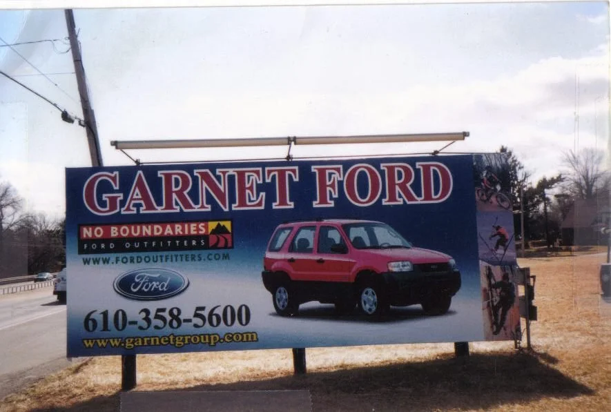 Billboard for Garnet Ford dealership with a red Ford SUV, contact number, website, and images related to outdoors and sports.