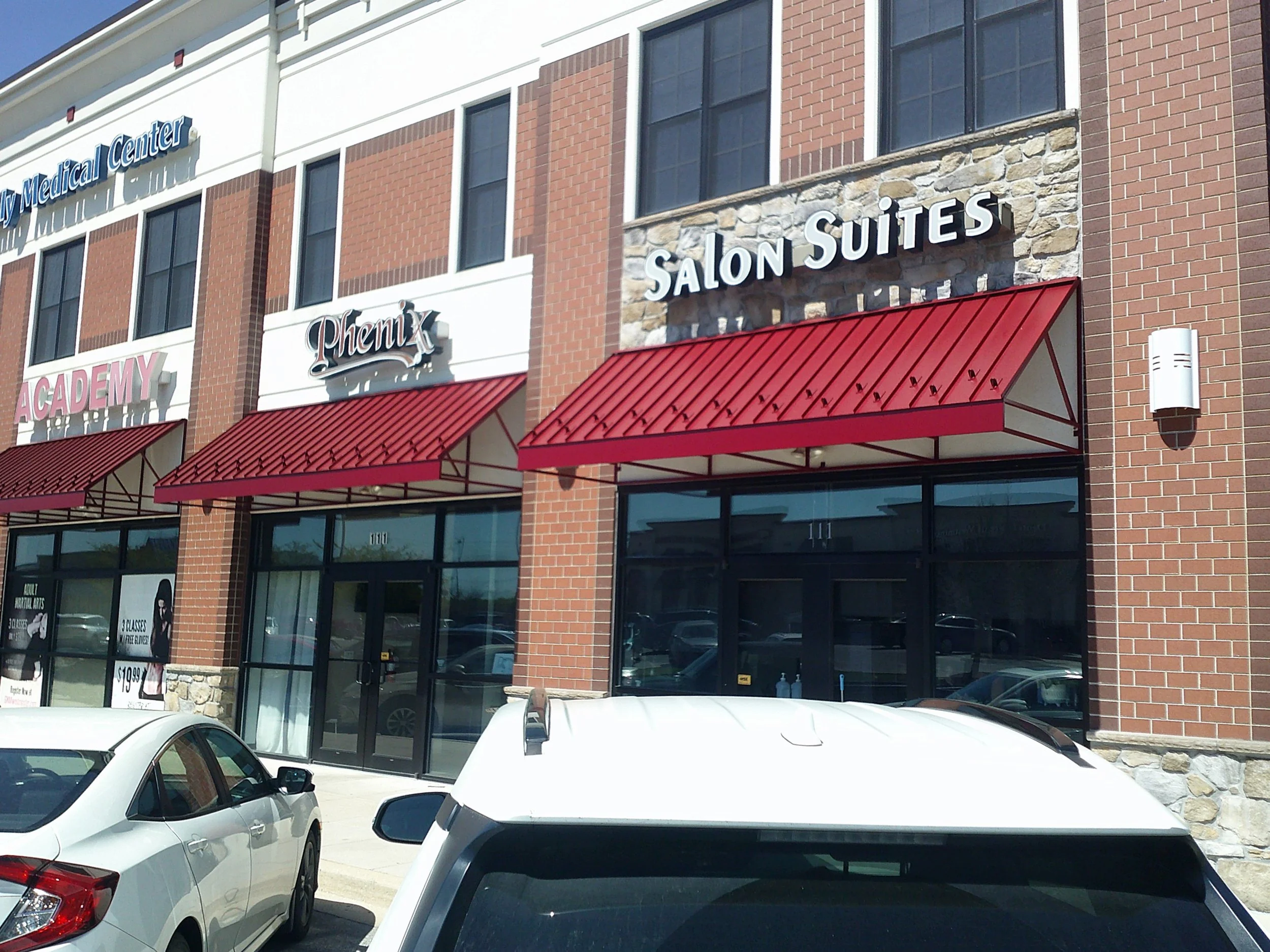 Front view of a multi-story medical office building with signs for 'Salon Suites' and other businesses, red awnings, and several white cars parked in front.