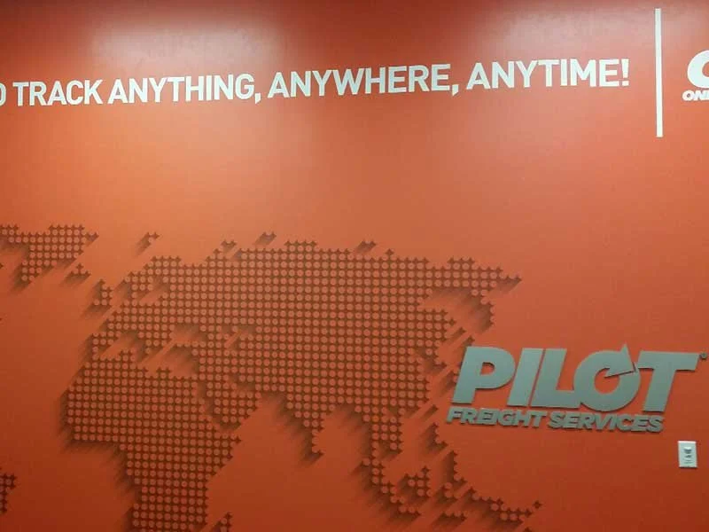 Red wall with a dotted world map, text promoting GPS tracking, and Pilot Freight Services logo.