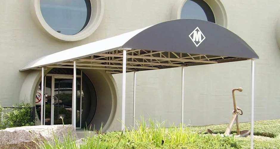 A modern building exterior with round windows, a curved entrance with a small awning, and a vintage bicycle sculpture in the landscaping.