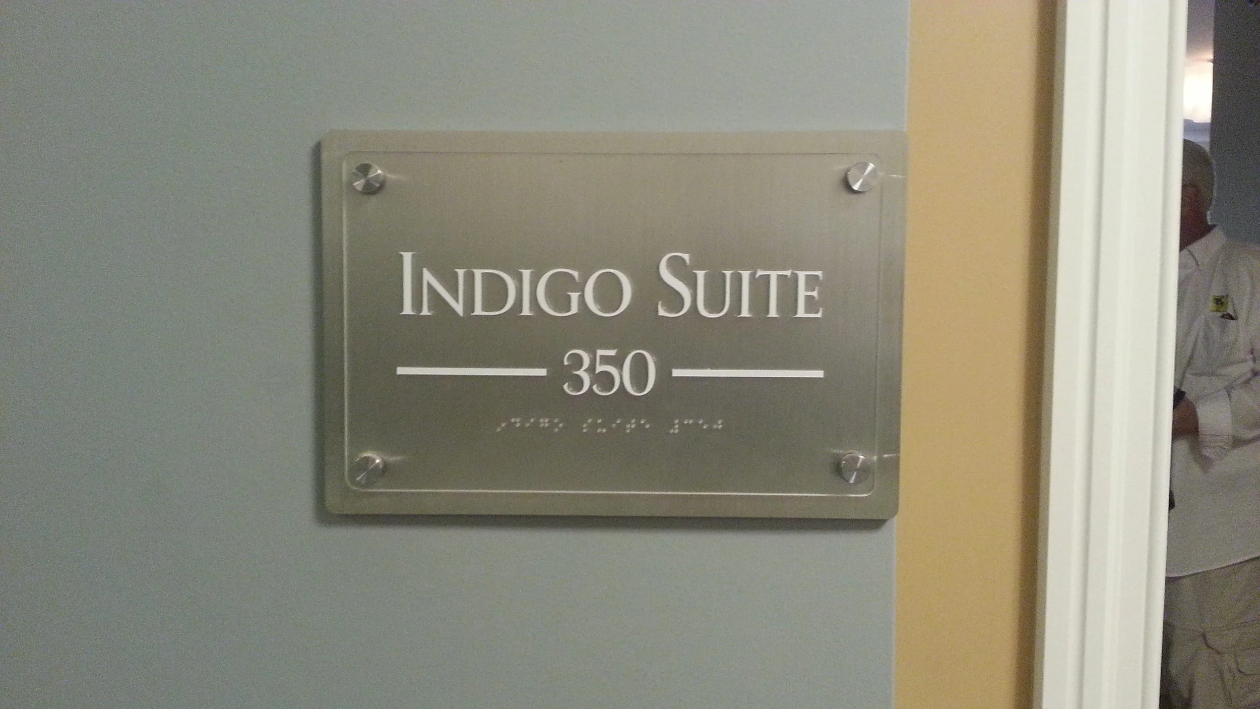 Sign on wall that reads 'Indigo Suite 350' with a person partially visible in the doorway to the right.