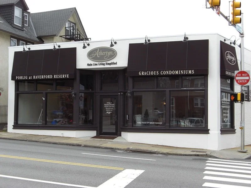 Commercial building with black awnings and signage for Ahheryn, advertising 'Main Line Living Simplified,' located at Pohlig at Haverford Reserve, promoting 'Gracious Condominiums.'