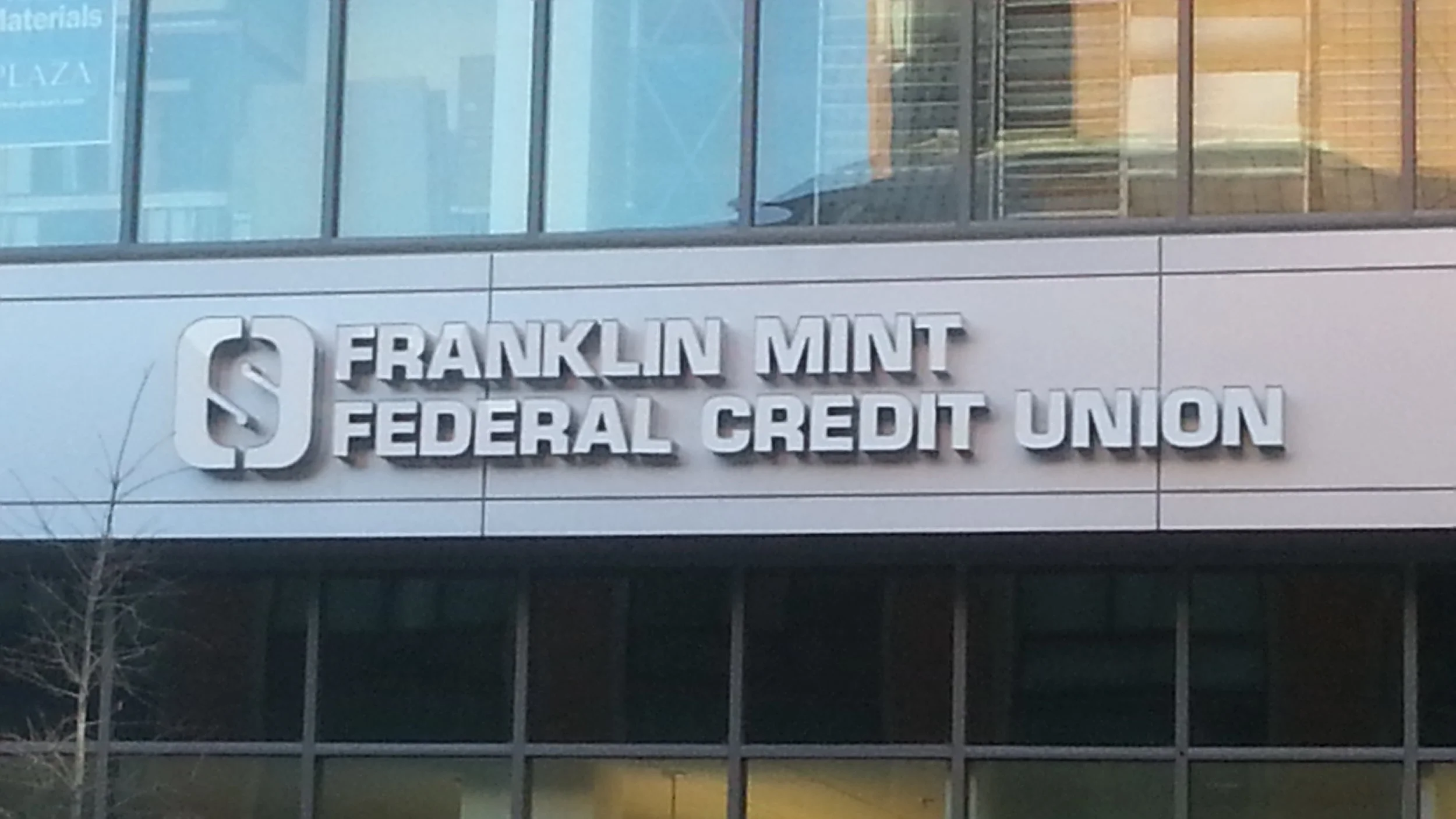 Sign for Franklin Mint Federal Credit Union on the exterior of a modern office building with glass windows.