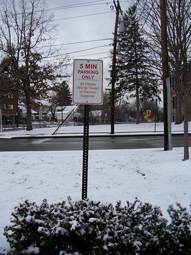 A parking sign in a snowy area indicating 5-minute parking only, with a warning that all others will be towed at the owner's expense.