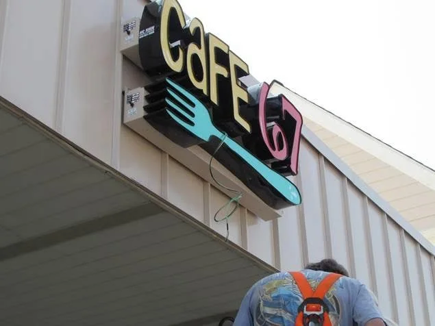 A sign for a cafe with a fork and knife icon, and the word 'CAFÉ' above the sidewalk with a person walking below.