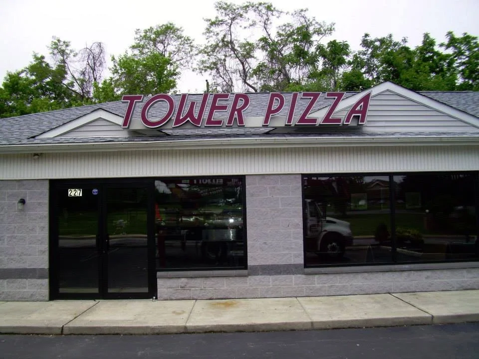 Exterior of a restaurant named Tower Pizza with a sign above the entrance and large windows.