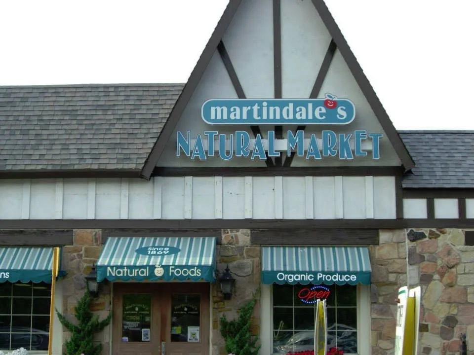 Exterior of a Martindale's Natural Market store with stone and wood siding, two green and white striped awnings, and a sign that reads 'Since 1869', 'Natural Foods,' and 'Organic Produce.'