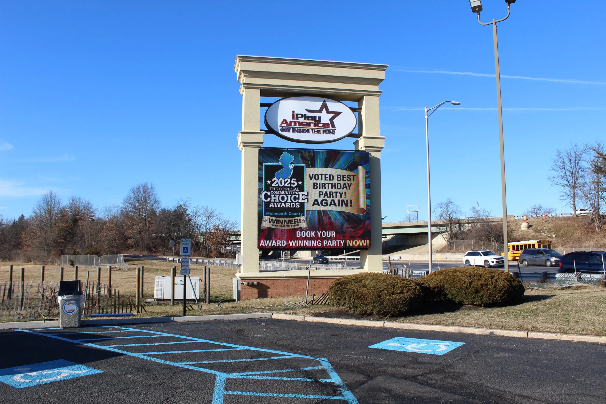 Parking lot with designated handicapped parking spaces and a large billboard advertising party venues, with a clear blue sky and some leafless trees in the background.