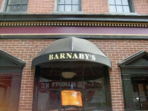 Barnaby's restaurant entrance with an awning and window, brick building facade, and a yellow notice on the window.
