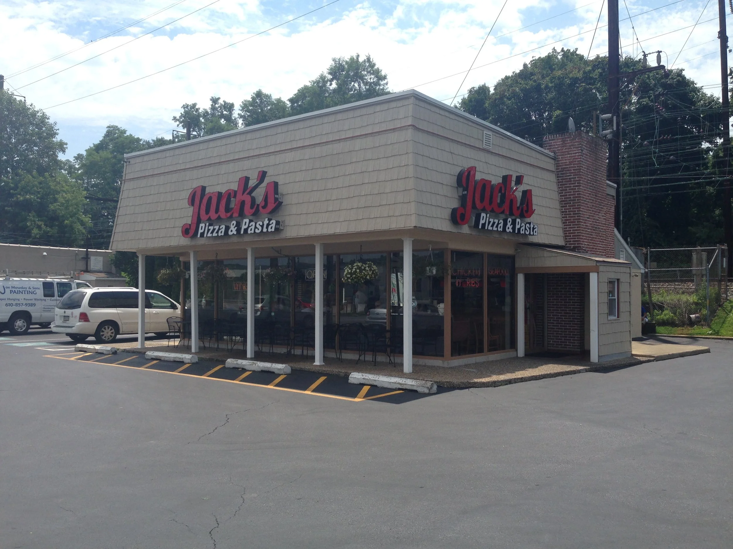 Exterior of Jack's Pizza & Pasta restaurant with beige siding, red and black sign, large windows, and a parking lot in front.