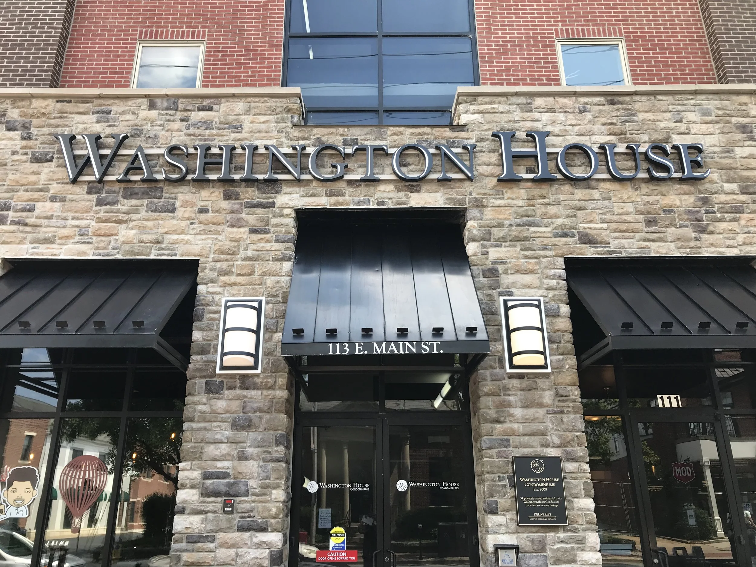 Front entrance to Washington House with a stone and brick facade, black signage, and windows. Street address 113 E. Main St. displayed above the door.