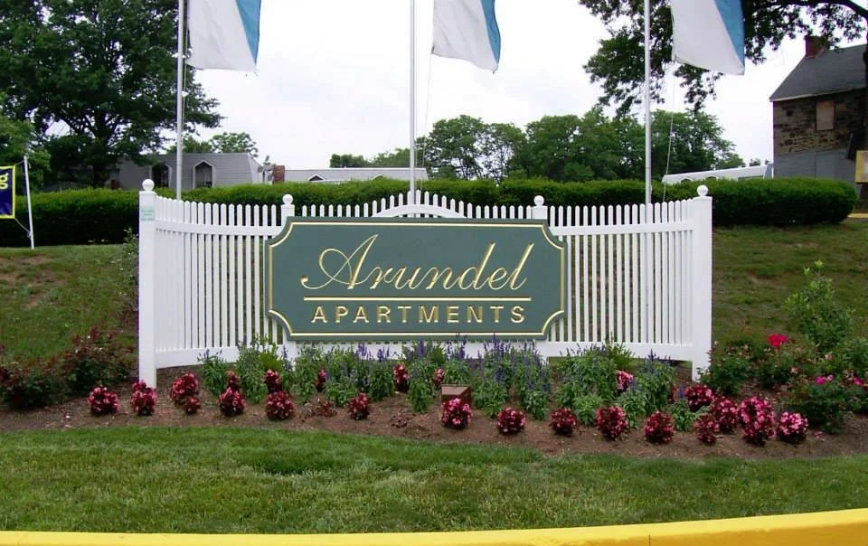 Sign for Arundel Apartments with white picket fence and flowerbed in front
