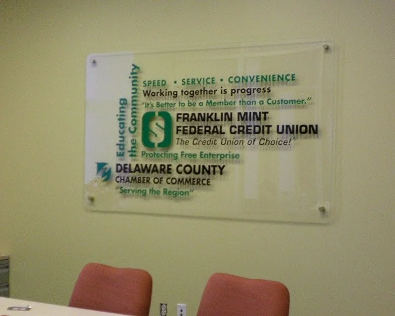 A wall-mounted sign for Franklin Mint Federal Credit Union and Delaware County Chamber of Commerce, emphasizing speed, service, and convenience with motivational quotes.