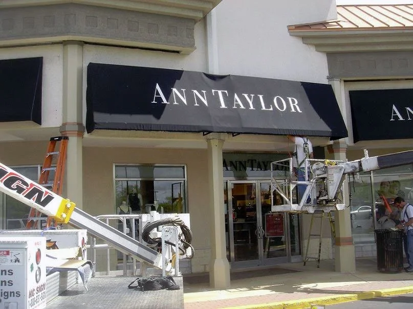 People working on renovation or maintenance outside a store with the sign 'ANTTAYLOR' on black awnings.