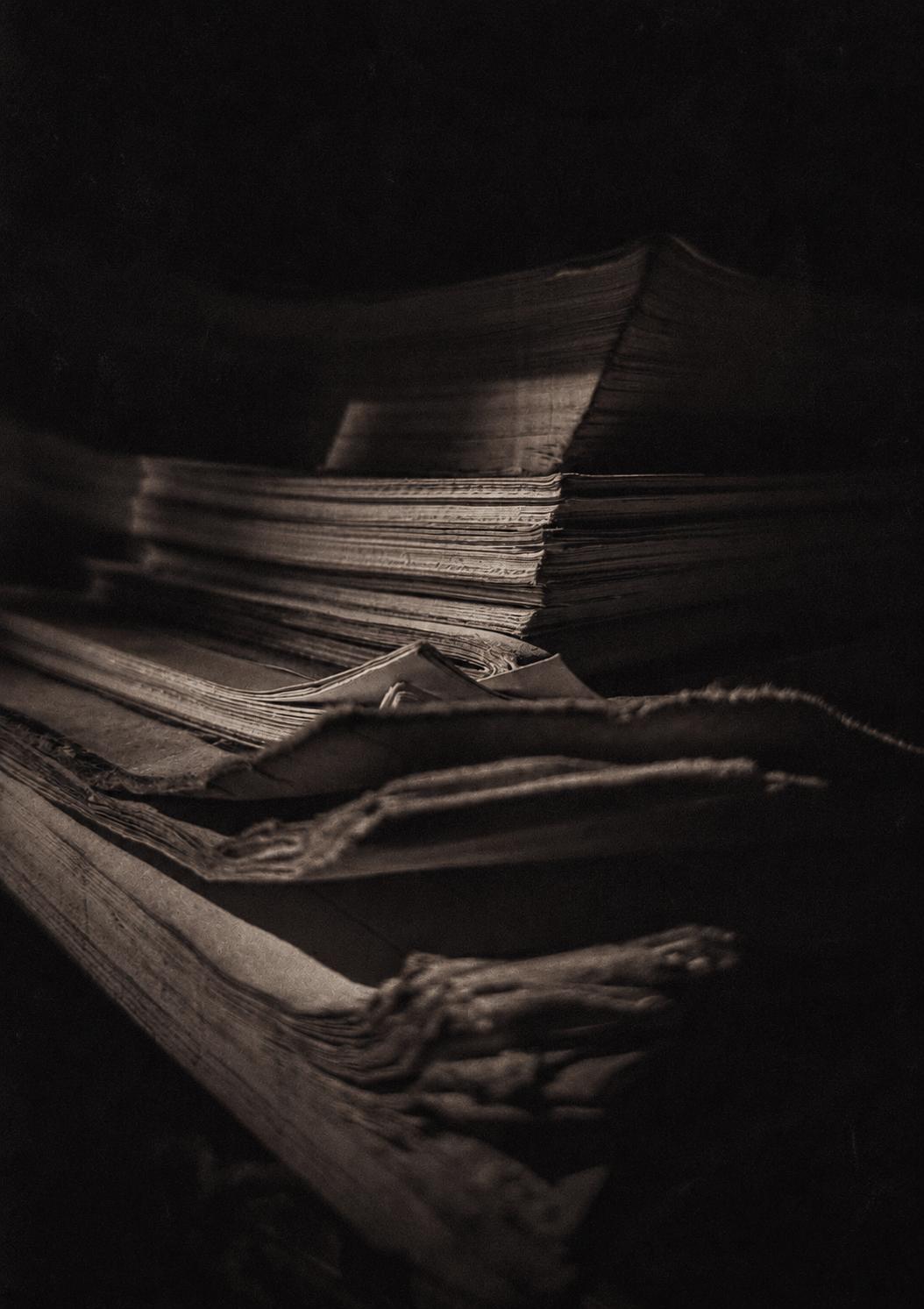 Close-up of old, worn books and papers stacked in a dimly lit environment.