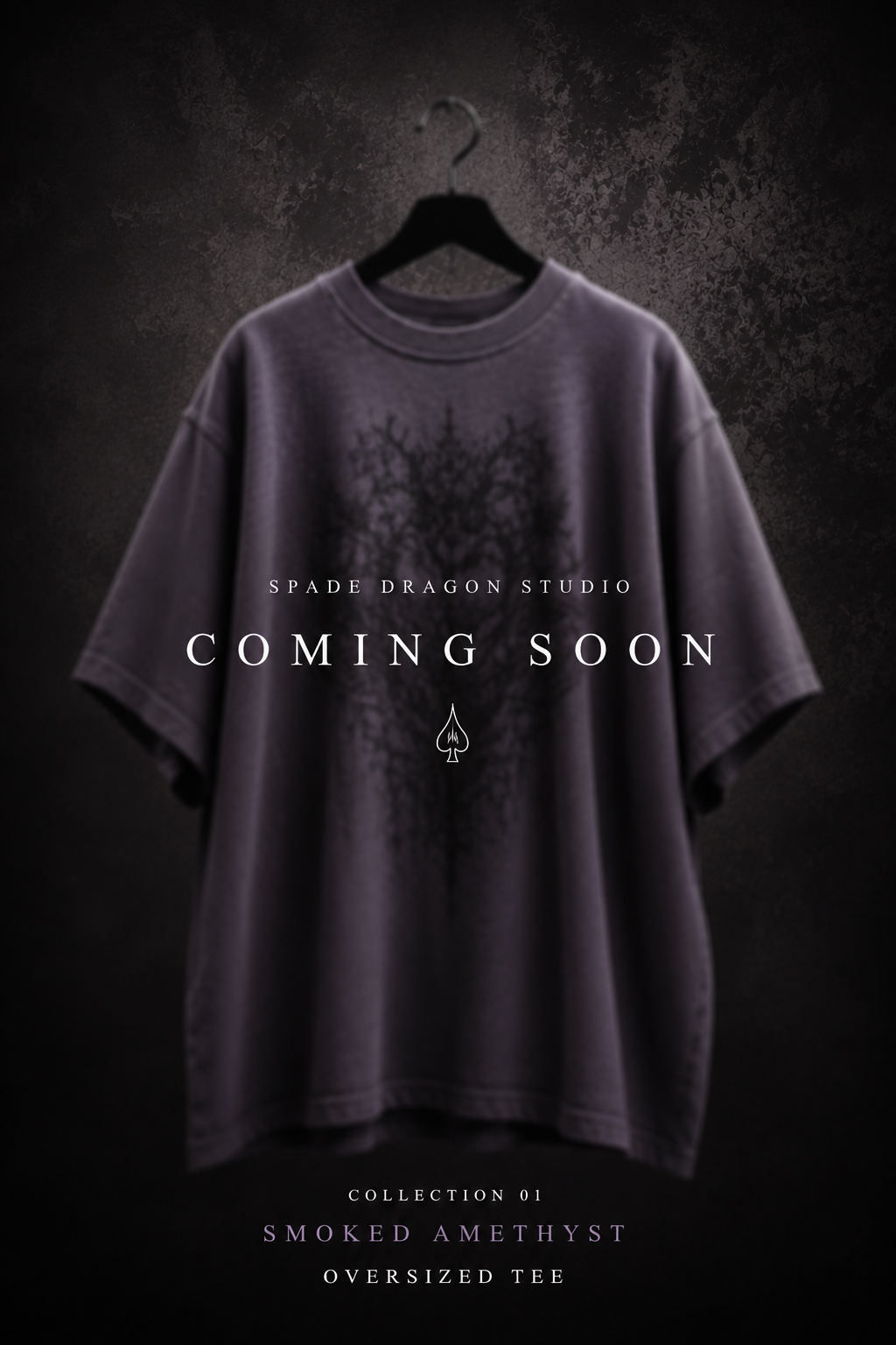 A dark oversized t-shirt with a black tree design hangs on a hanger against a dark textured background. The text overlay reads "Spade Dragon Studio Coming Soon" with an icon of a spade symbol below, and additional text at the bottom says "Collection 01 Smoked Amethyst Oversized Tee."