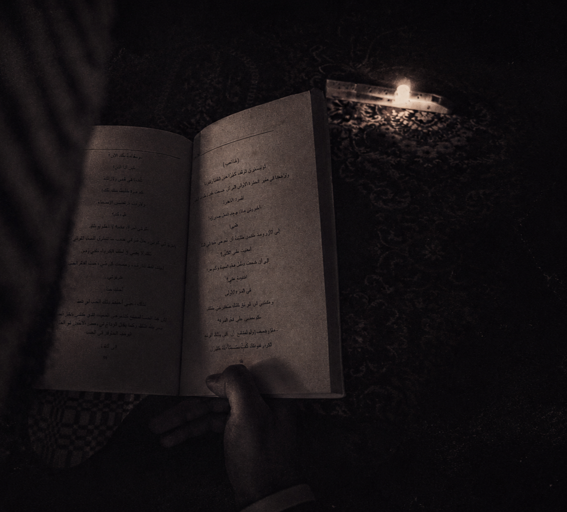 Person reading an open book illuminated by a small candle on a dark surface.