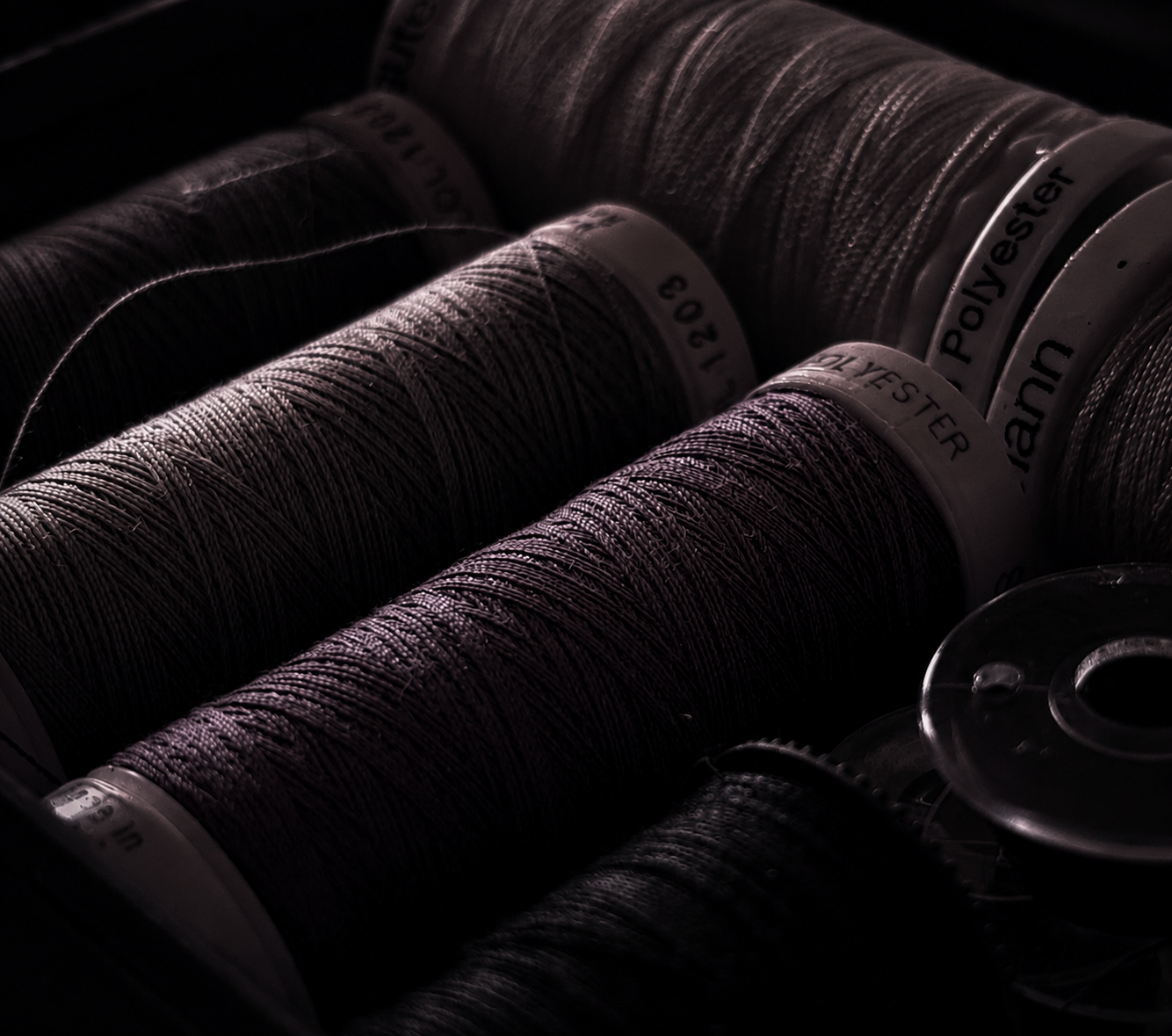 Close-up of multiple spools of sewing thread in dark lighting.