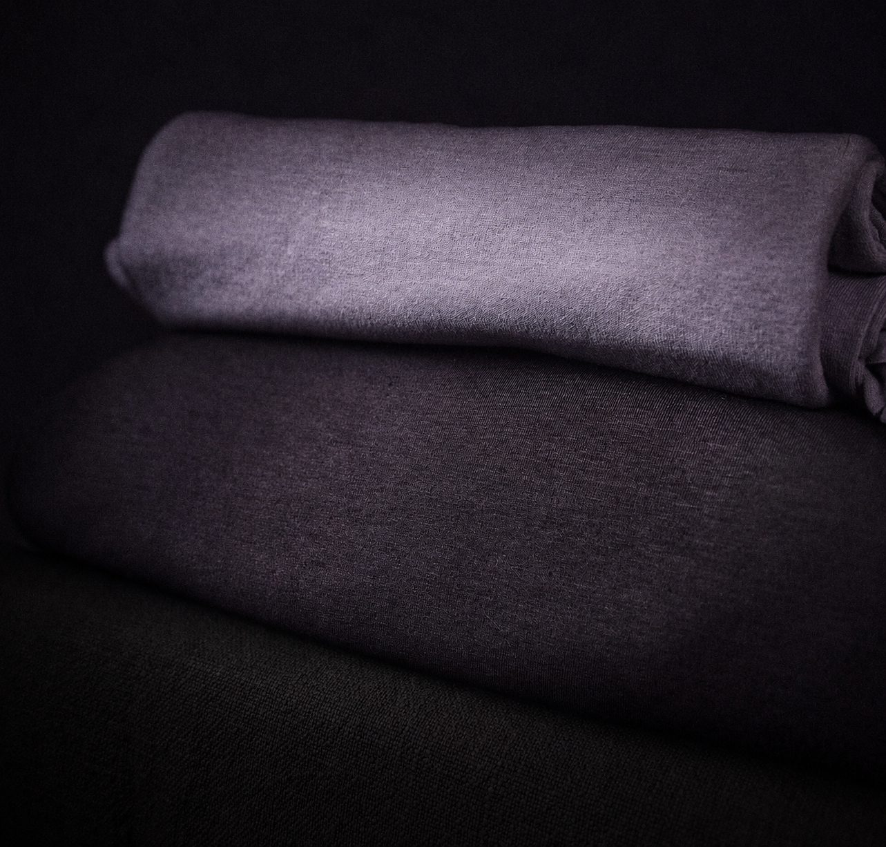 Folded gray and dark gray fabric or clothing on a dark surface.