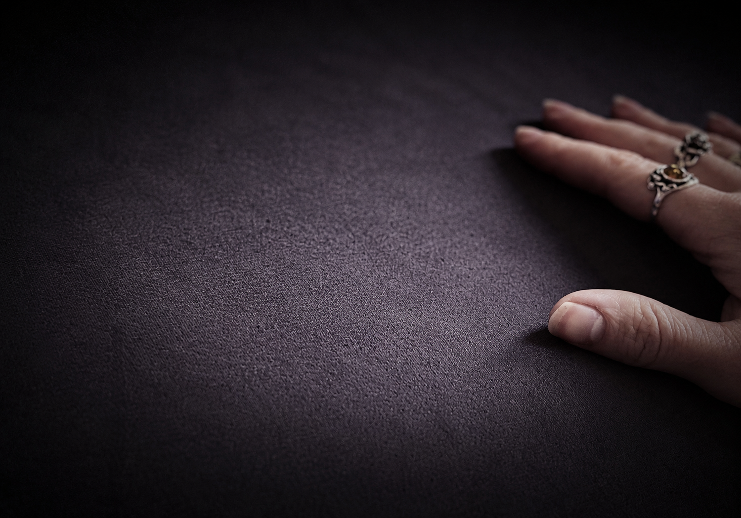 A person's hand with fingernails and rings resting on a dark textured surface.