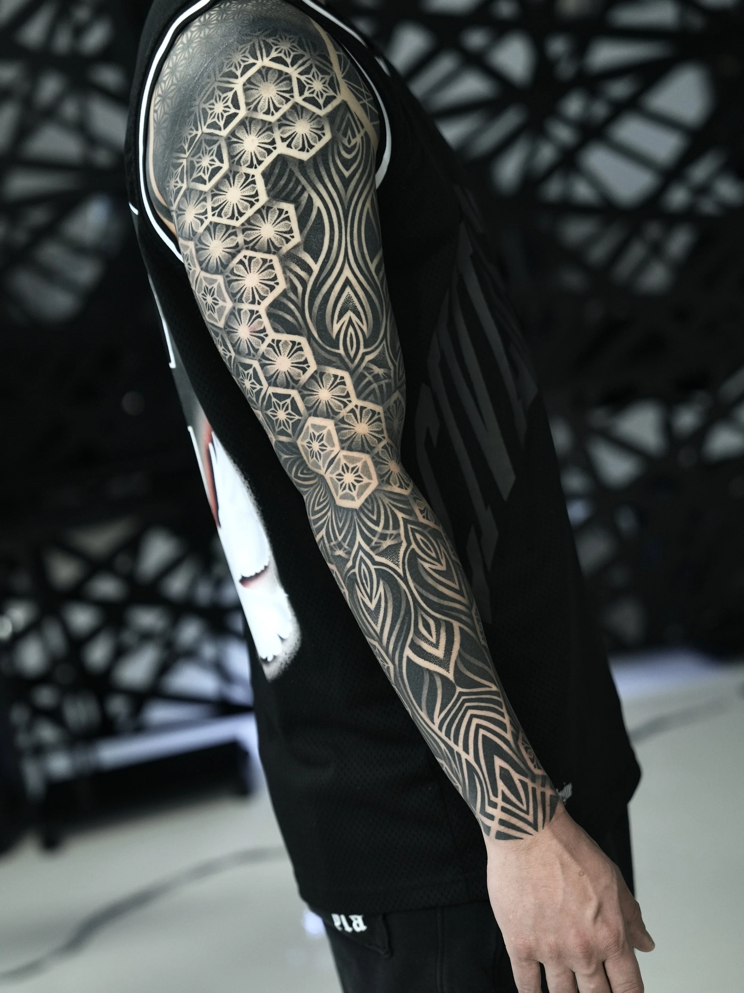 A person's arm with a detailed black geometric tattoo extending from shoulder to wrist.