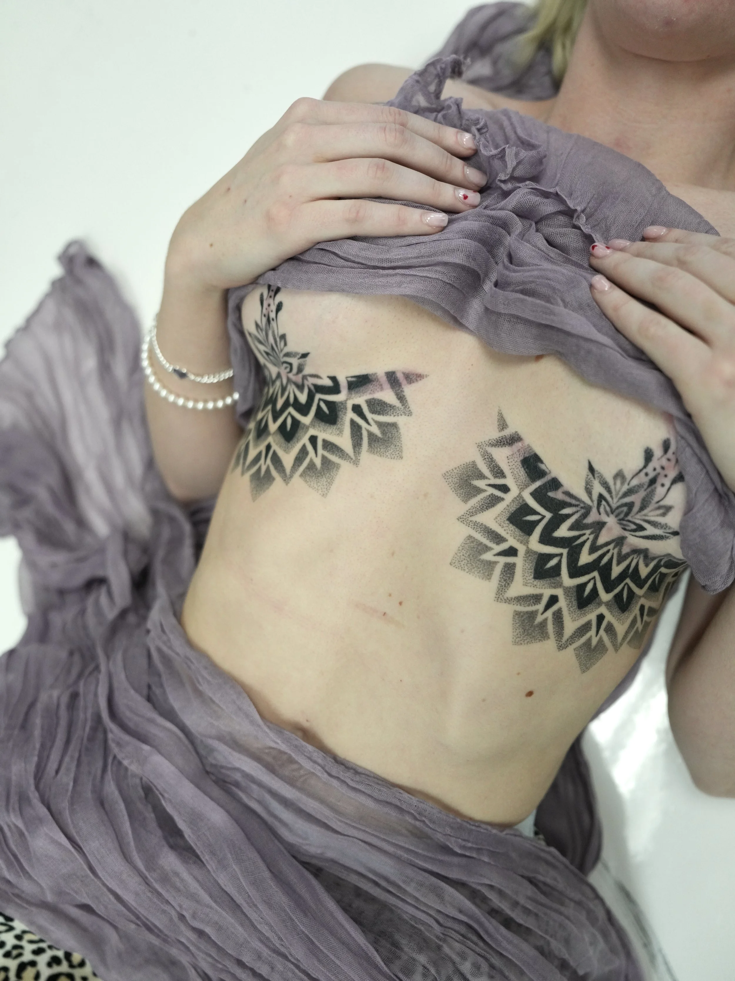 A woman lifting her purple dress to reveal black geometric tattoos on her ribcage.