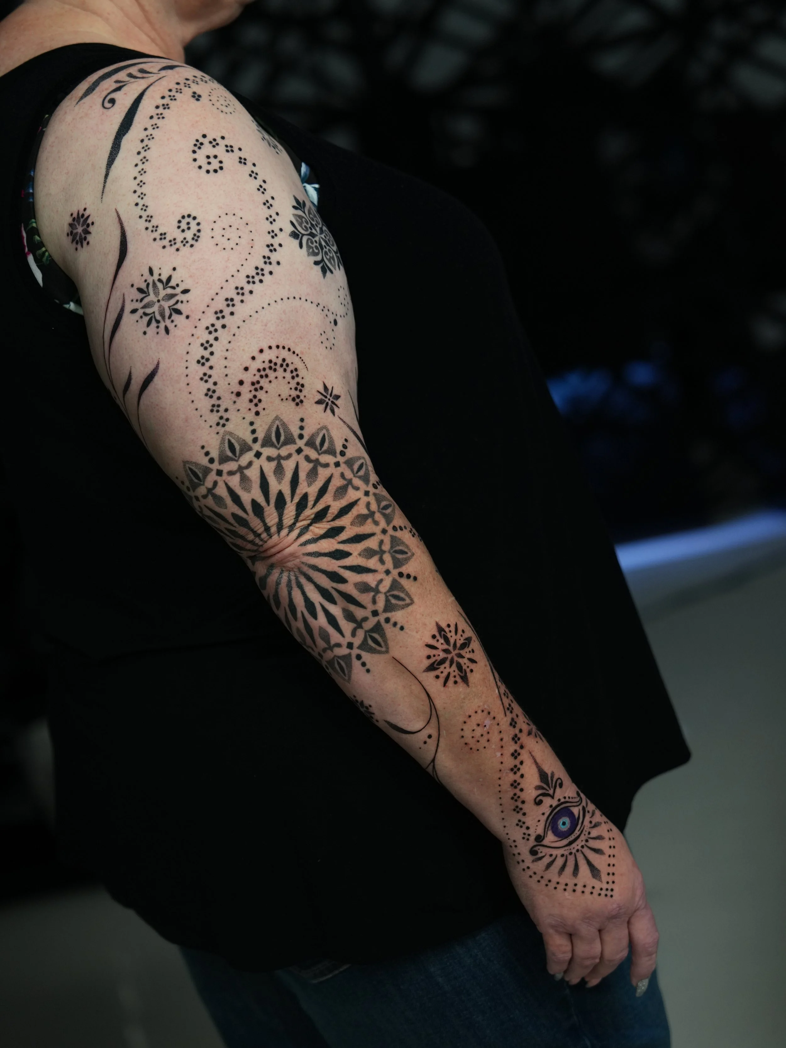 Close-up of a person's arm with a detailed black tribal-style tattoo featuring geometric and floral patterns, including an eye design near the wrist.