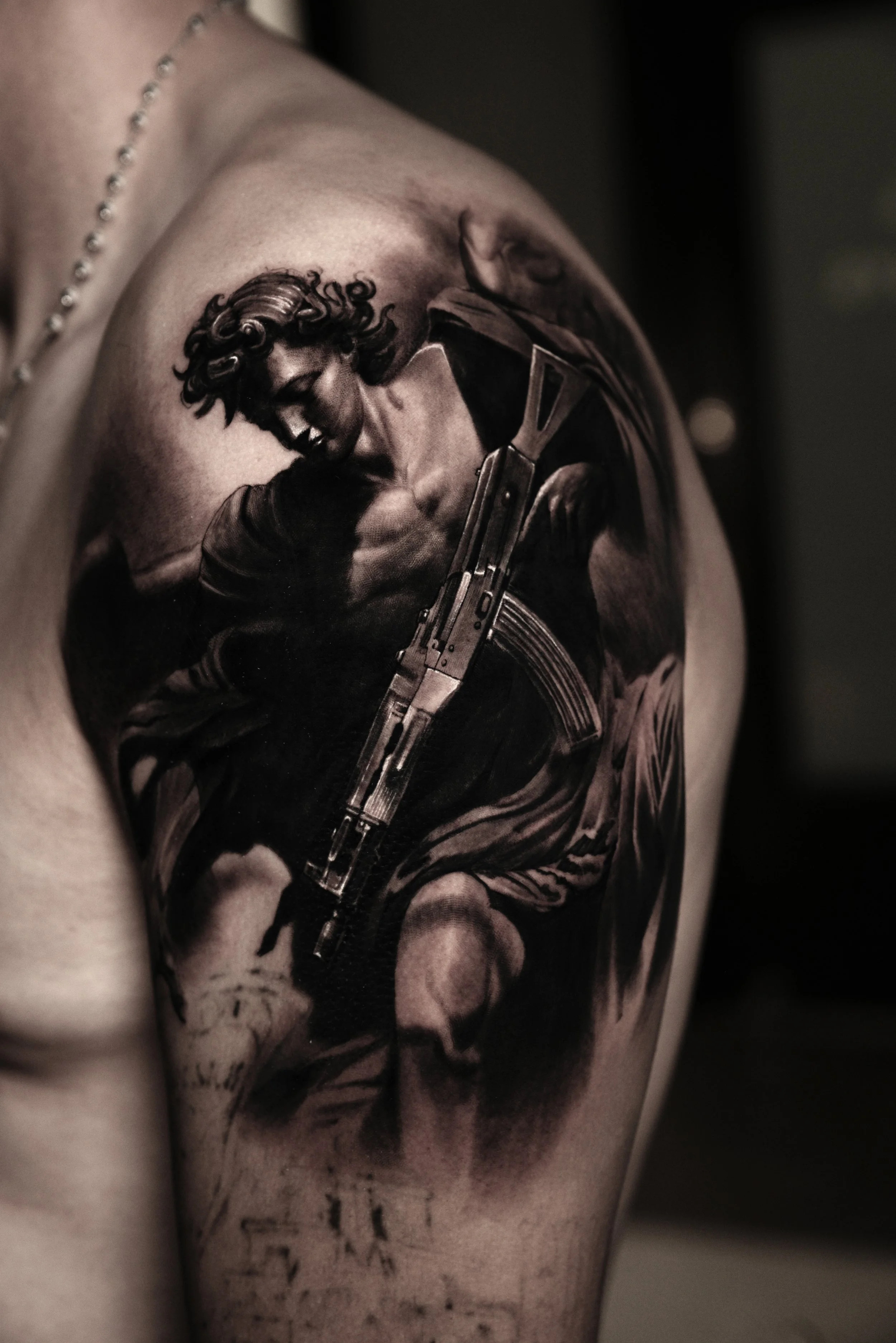 A black and gray tattoo of a woman with curly hair, smiling, holding a revolver, on an arm.