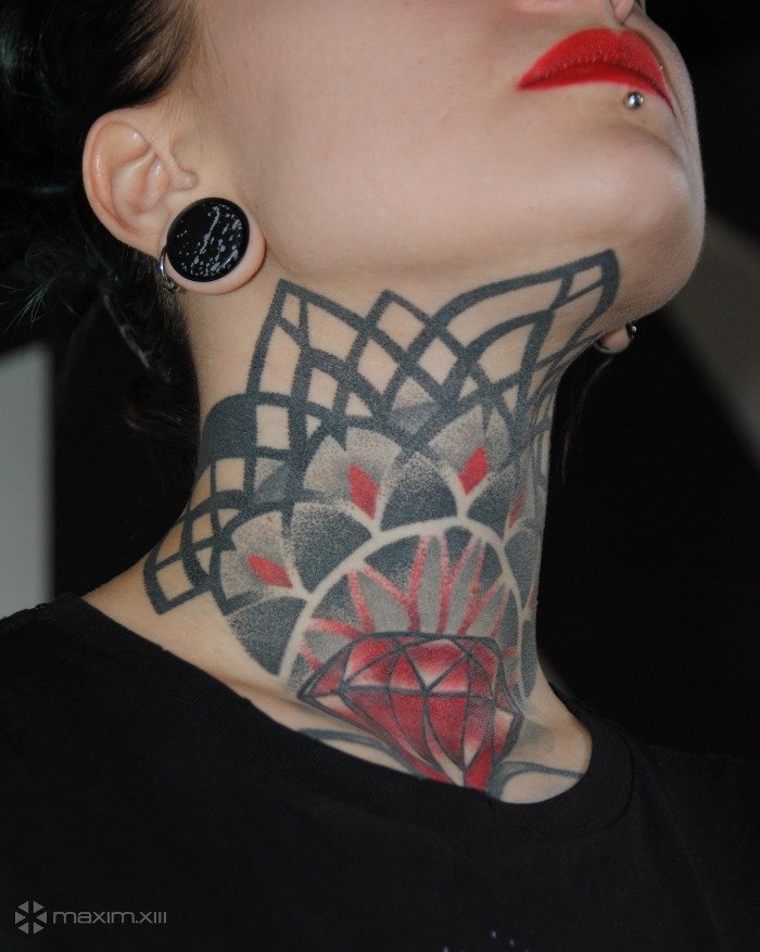 Close-up of a person's neck tattoo featuring geometric and floral patterns, a red diamond shape, and part of their face with red lipstick and a tongue piercing.