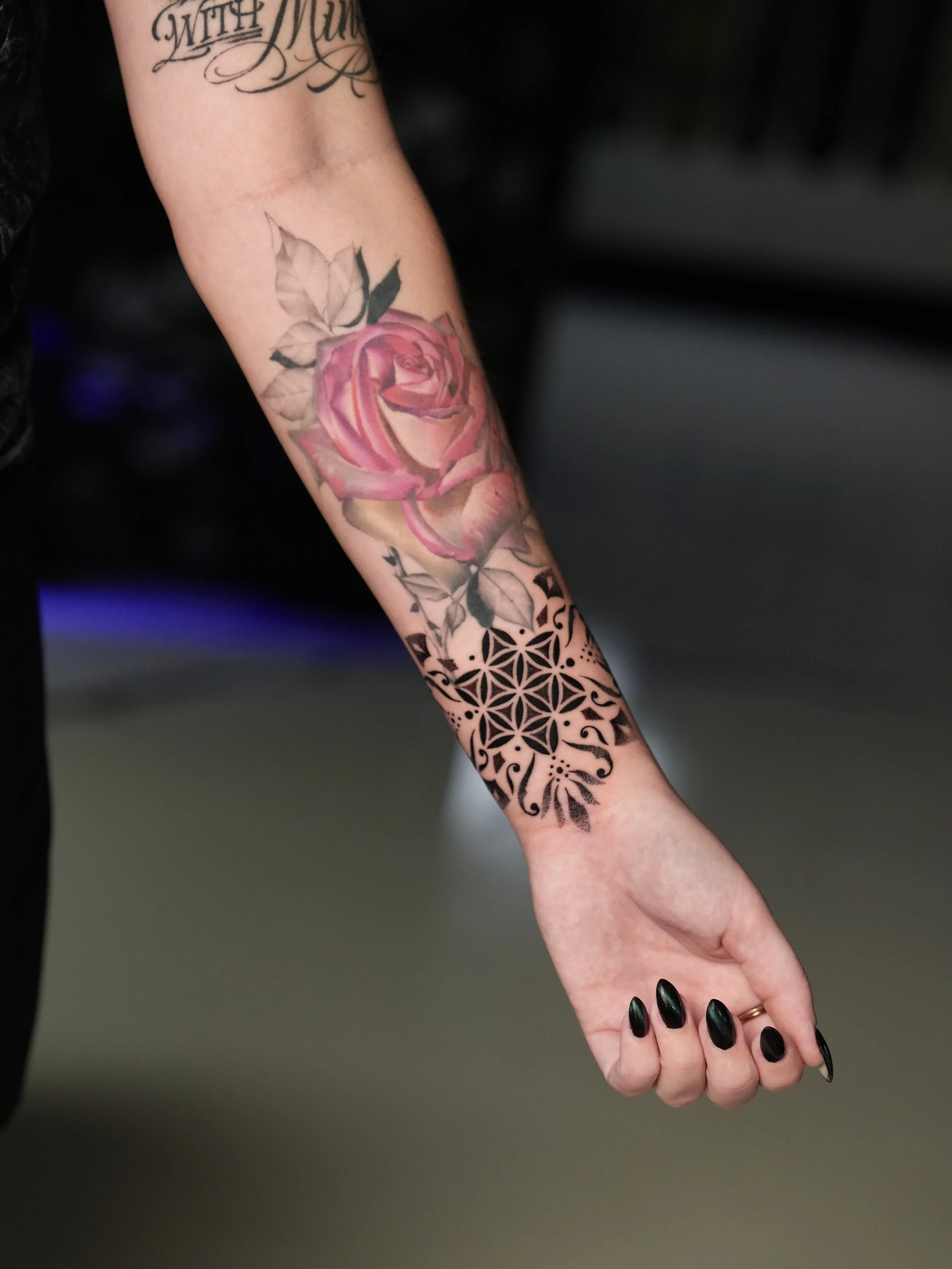Tattooed arm with a pink rose and black geometric and floral designs.