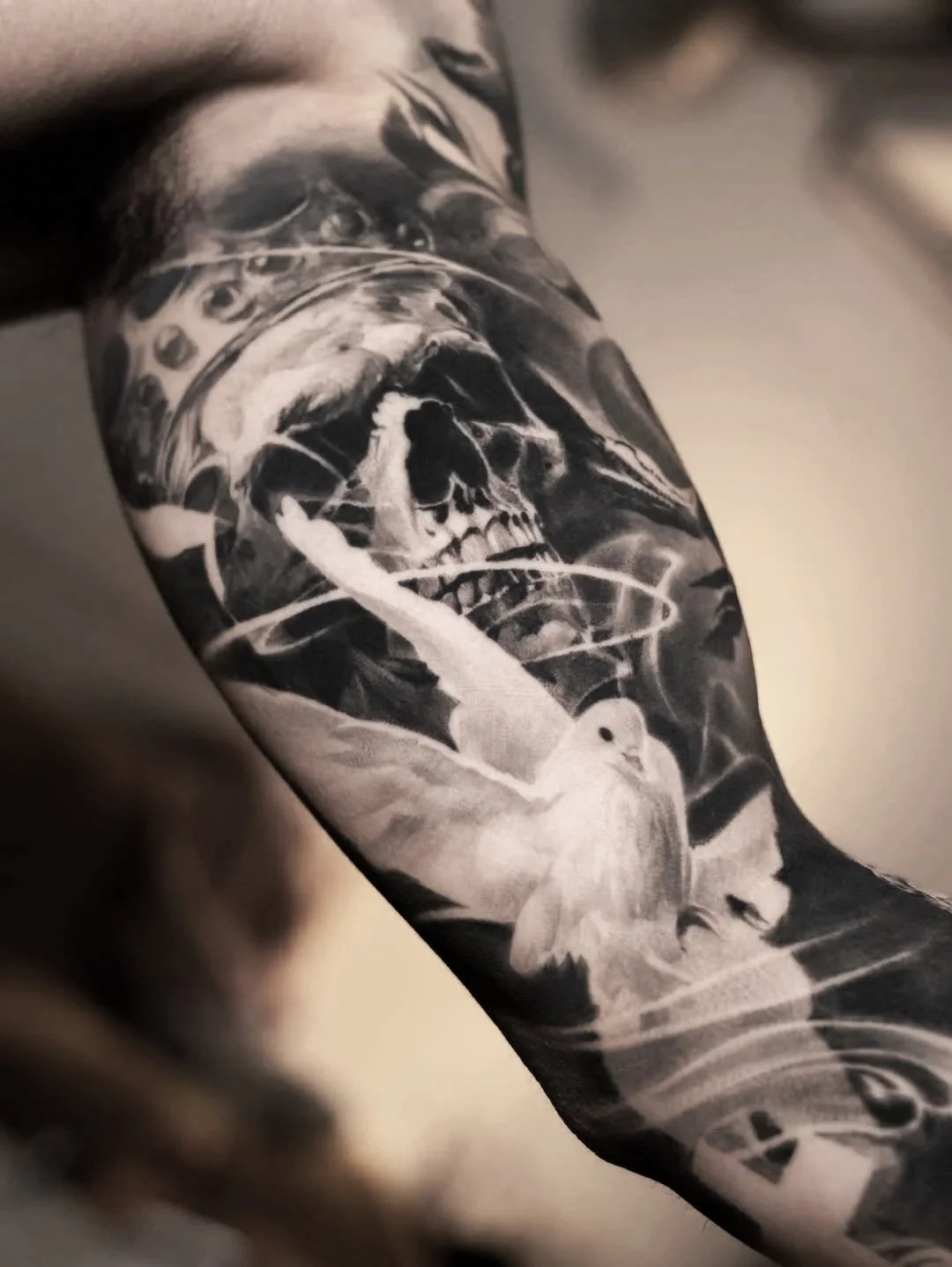 Close-up of a tattoo featuring a detailed skeleton face, a white dove, and abstract elements in black and white.
