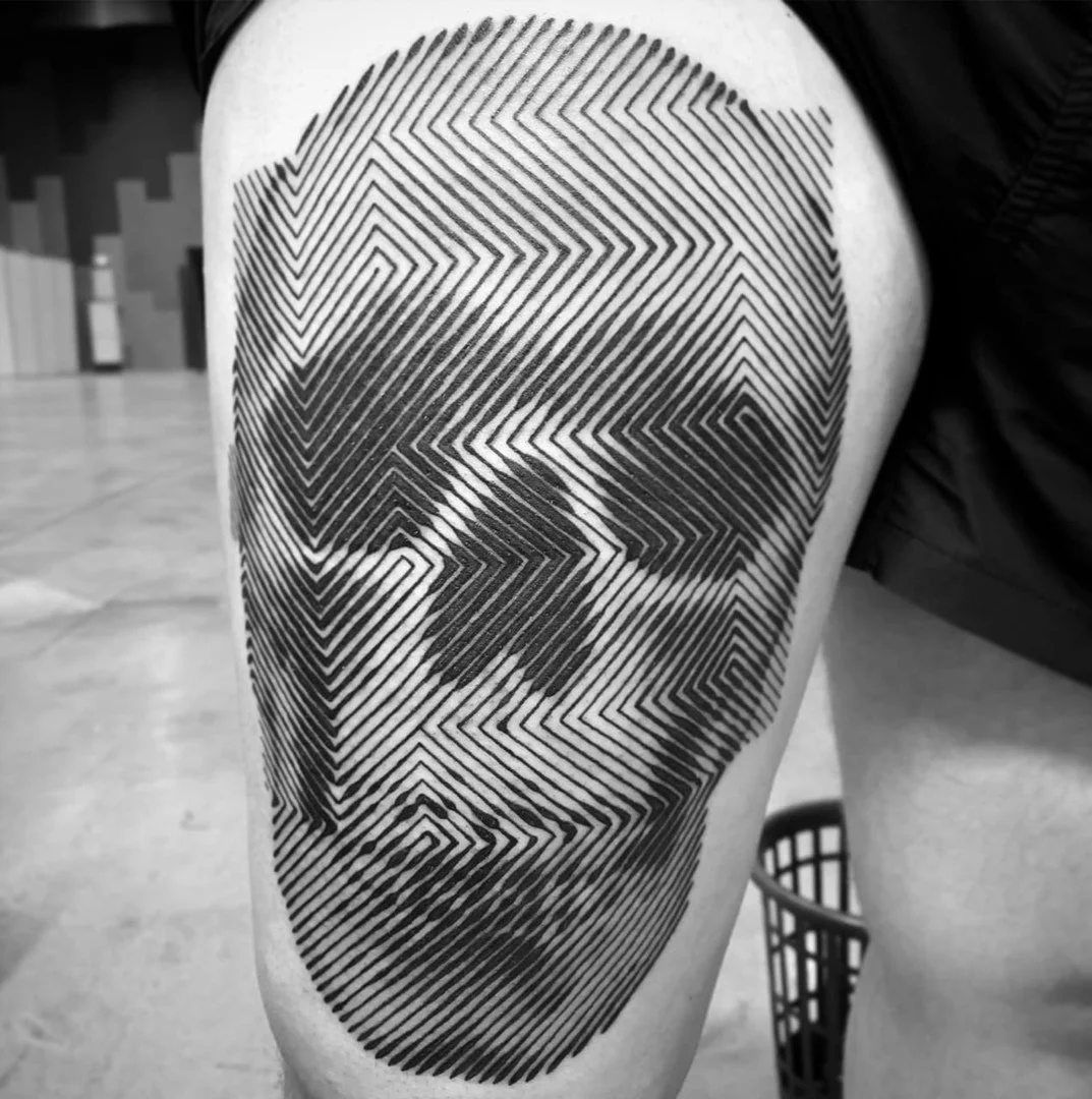 Tattoo of a human face created with black diagonal lines on a person's thigh