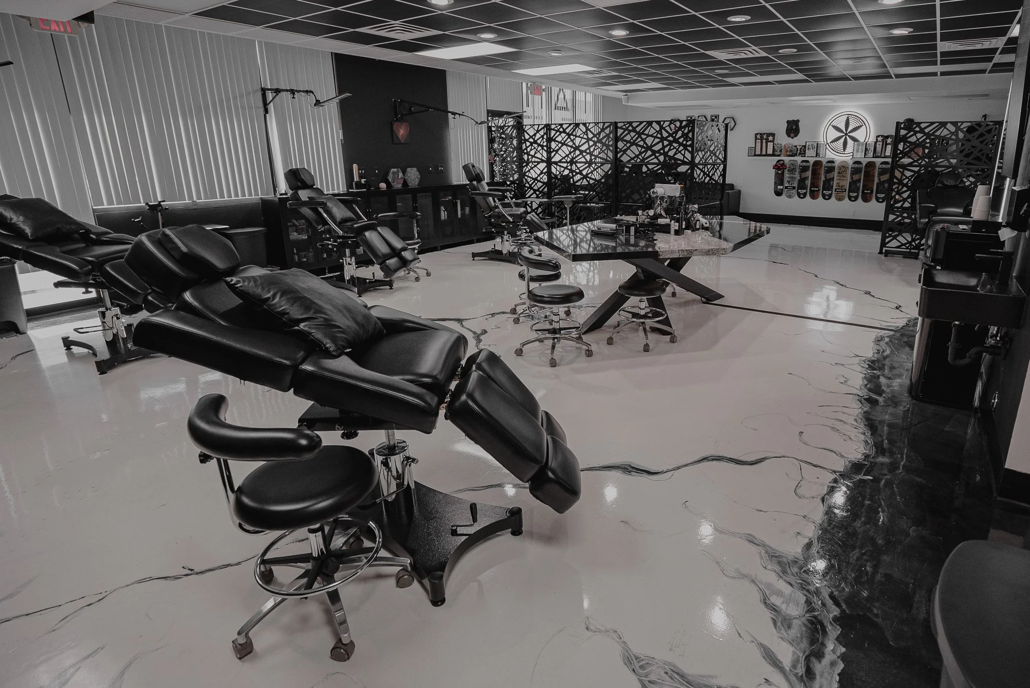 Inside a modern tattoo parlor with black reclining chairs, a marble table, and skateboards on the wall.