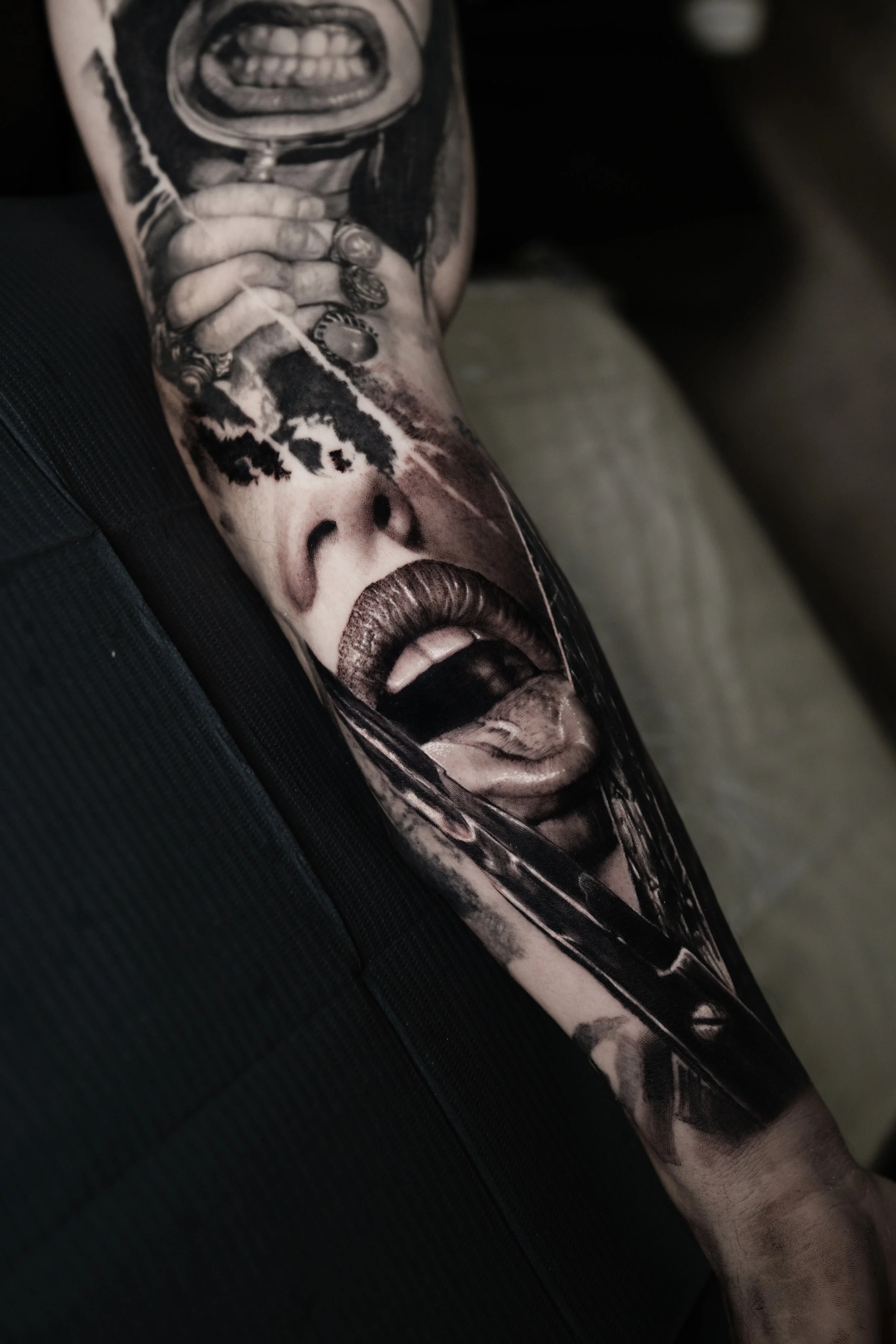 A tattoo sleeve featuring a woman with open mouth, detailed with various elements including a hand with rings, black ink splatters, and realistic shading.