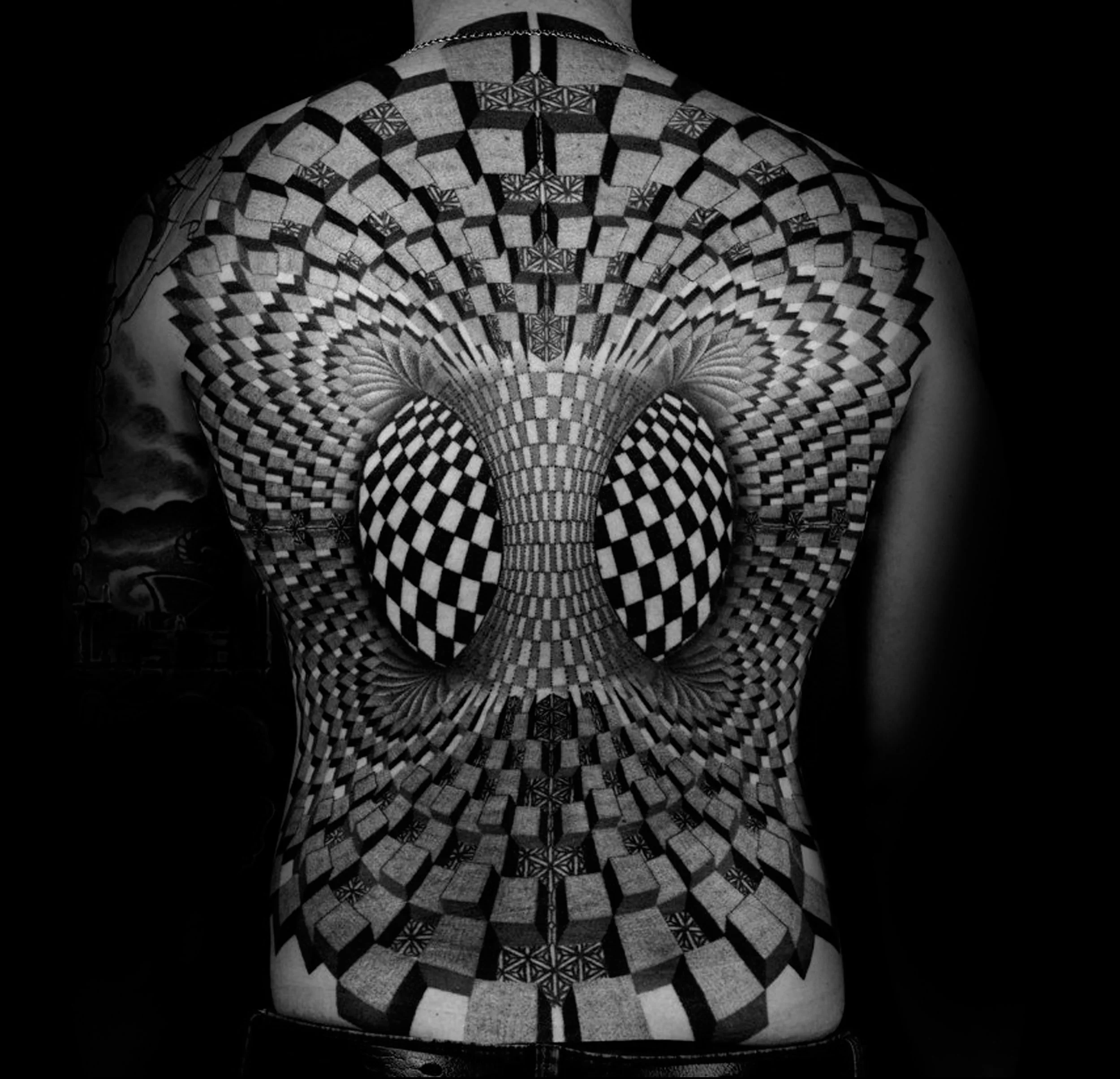 A person's back features a large black and white geometric tattoo with a 3D optical illusion pattern, creating a vortex effect.