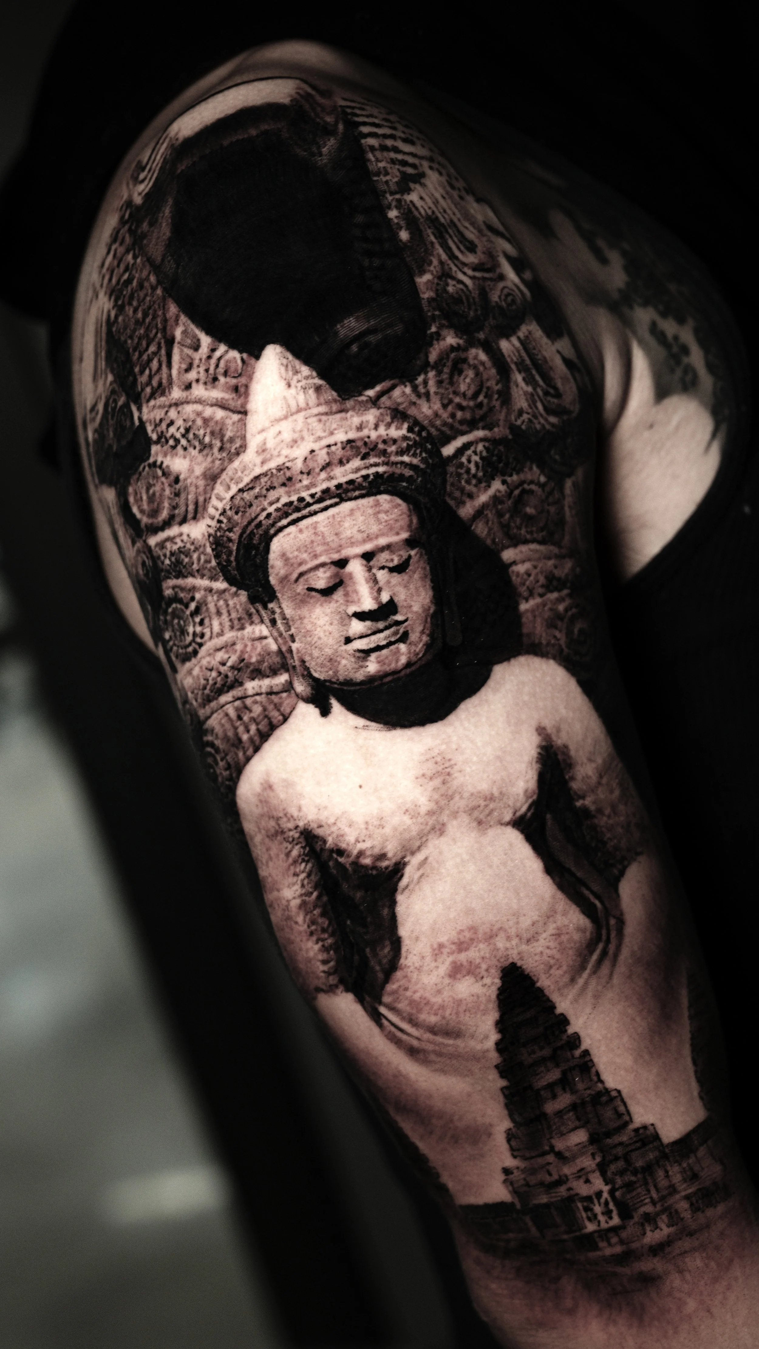 A tattoo of a Buddha figure with a cityscape below, featuring detailed shading and design.