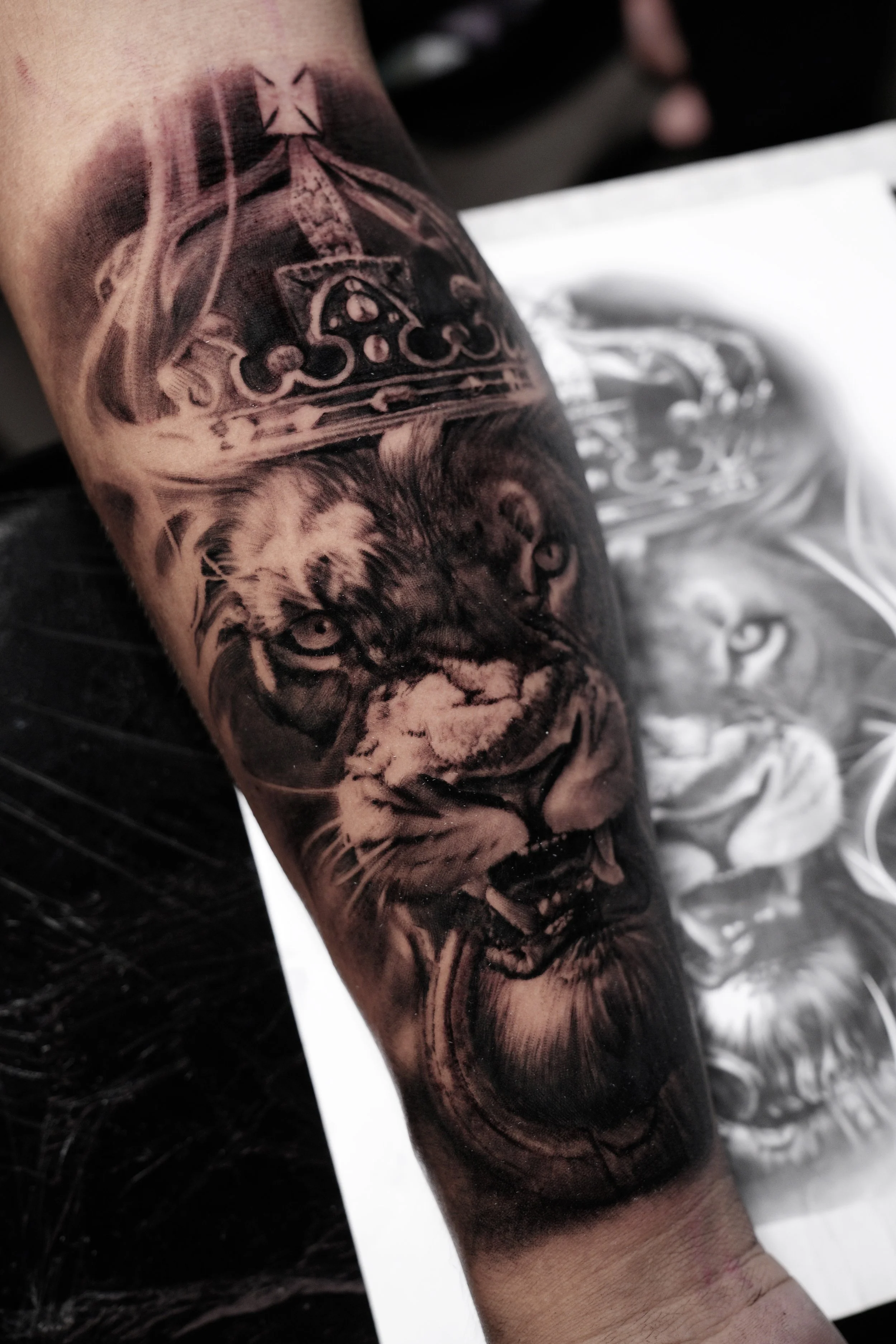 Black and gray realistic tattoo of a tiger's face and a crown on the person's arm.